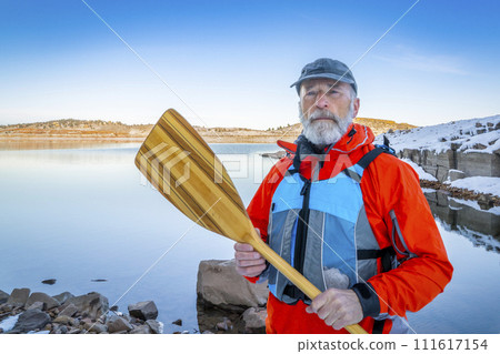 senior canoe paddler wearing life jacket on a shore of Carter Lake in northern Colorado in winter scenery 111617154