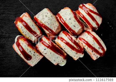 Top view of sushi rolls topped with peanut and unagi sauces on black 111617569