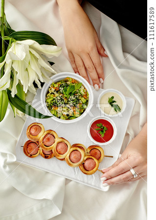 Female hand taking sausage rolls on skewers from plate during romantic dinner 111617589