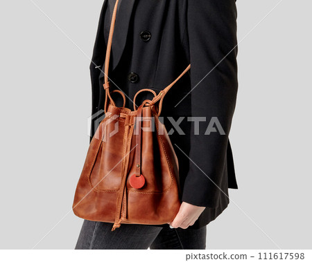 Stylish woman in black jacket holding brown leather drawstring bag Stylish woman in black jacket holding brown leather drawstring bag 111617598