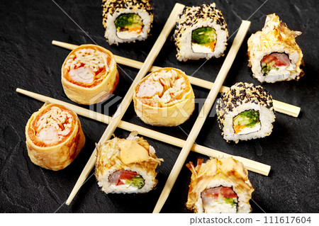 Sushi rolls and chopsticks arranged in tic-tac-toe game on black 111617604