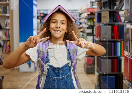 Portrait of happy girl child with opened diary on head gesturing peace sign 111618336
