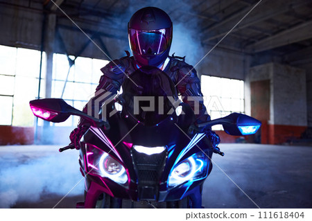 Front view portrait of motor biker driving sport motorcycle in neon light Front view portrait of motor biker driving sport motorcycle in neon light 111618404