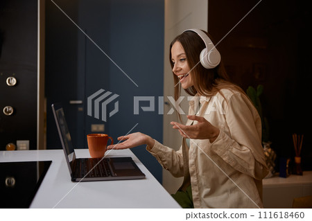 Young woman wearing headphones having meeting on laptop from home Young woman wearing headphones having meeting on laptop from home 111618460