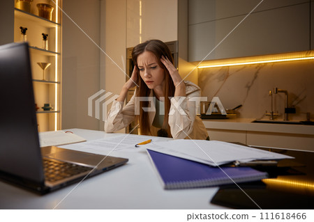Overwhelmed woman touching head in panic sitting front of laptop at home Overwhelmed woman touching head in panic sitting front of laptop at home 111618466