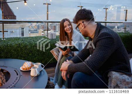 Young girlfriend reading for boyfriend while couple resting at roof top cafe Young girlfriend reading for boyfriend while couple resting at roof top cafe 111618469