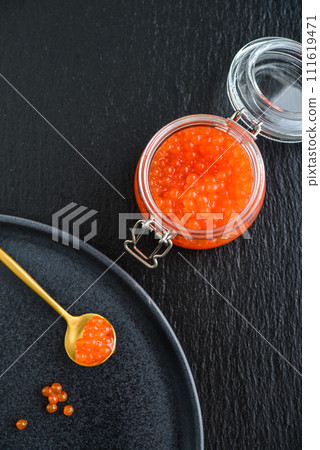 Red caviar in the glass jar on black slate  background 111619471