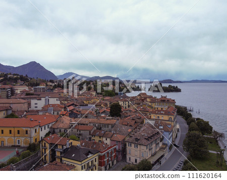 View of a city with colorful buildings, parked cars, and mountains Lago Maggiore 111620164