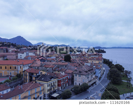 View of a city with colorful buildings, parked cars, and mountains Lago Maggiore 111620166