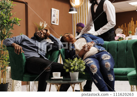 Tired, stressed jetlagged hotel guests sleeping in lobby, taking rest after long flight. Exhausted travellers taking nap having jet lag symptoms, african american couple sleep after arrival at resort 111620263