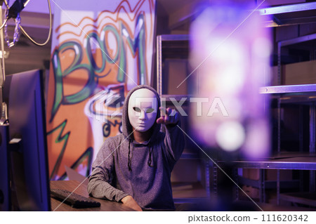Anonymous man pointing at mobile phone camera while recording ransom video. Criminal streaming threat on smartphone while breaking law and doing illegal activity in abandoned warehouse 111620342