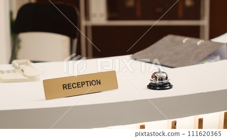 Close up of hotel lounge check in reception in brand new opening resort awaiting guests. Concierge bell, tourists accommodation info folder and phone on motel counter desk 111620365