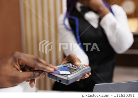 Hospitality and NFC technology. Close up of male hand holding credit card paying for room during check-in at front desk, receptionist receiving cashless payment from guest in hotel Hospitality and NFC technology. Close up of male hand holding credit card paying for room during check-in at front desk, receptionist receiving cashless payment from guest in hotel 111620391