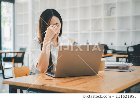 Business and technology concept, A stressed young female professional is rubbing her forehead while looking at a laptop screen in a modern workspace setting. Business and technology concept, A stressed young female professional is rubbing her forehead while looking at a laptop screen in a modern workspace setting. 111621953