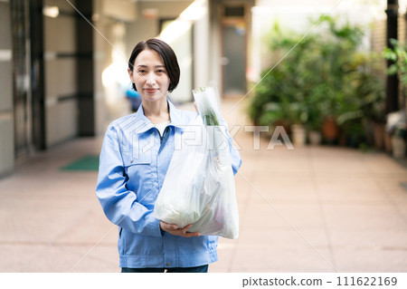 A woman wearing work clothes and holding a supermarket bag 111622169