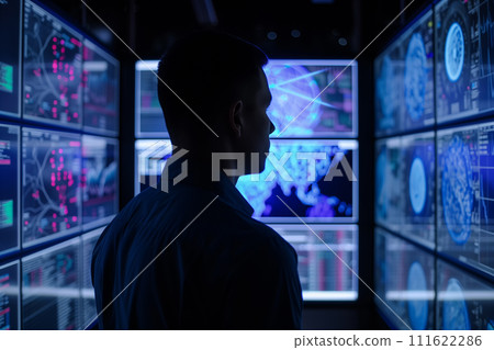 Silhouette of a man analyzing complex data across multiple high-tech computer monitors in a dark control room. 111622286