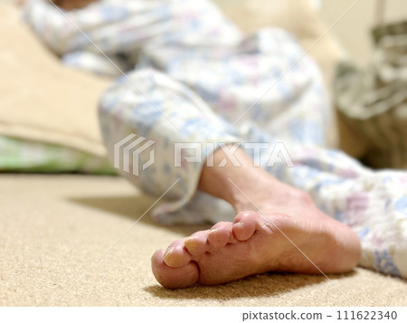 The soles of the feet of an elderly woman in nightwear lying on a folded futon 111622340