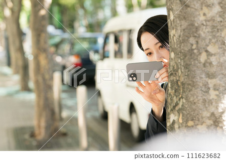 A female reporter in a suit secretly taking pictures with a smartphone 111623682