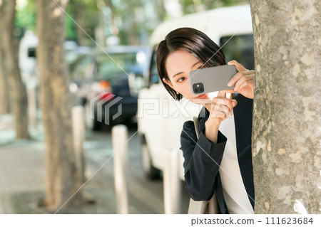 A woman in a suit taking secret pictures with her smartphone A woman in a suit taking secret pictures with her smartphone 111623684