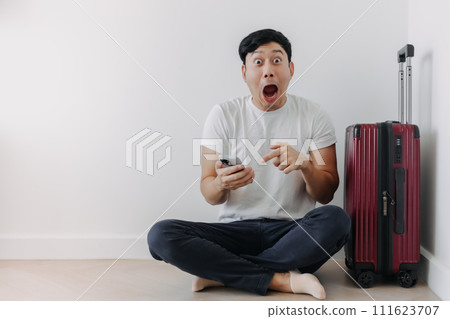 Shock and surprise face of man using mobile phone application for travel, sitting with his baggage or luggage. Shock and surprise face of man using mobile phone application for travel, sitting with his baggage or luggage. 111623707