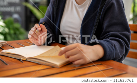A cropped shot of a woman writing down her ideas in a book while sitting in a cafe. A cropped shot of a woman writing down her ideas in a book while sitting in a cafe. 111623761