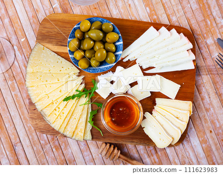 On wooden table there is cutting board with assorted cheese, honey, pickled olives - On wooden table there is cutting board with assorted cheese, honey, pickled olives - 111623983