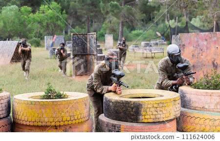 Men and women in protective uniform playing paintball on shooting range outdoor 111624006