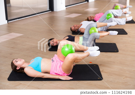 Group of people performs a twisting exercise, clomped a miniball between their knees Group of people performs a twisting exercise, clomped a miniball between their knees 111624198