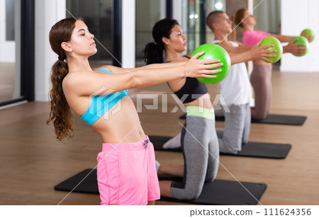 Sports people perform an exercise holding a mini Pilates ball in front of them Sports people perform an exercise holding a mini Pilates ball in front of them 111624356
