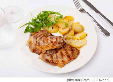 Fried pork served with potatoes and arugula 111624360