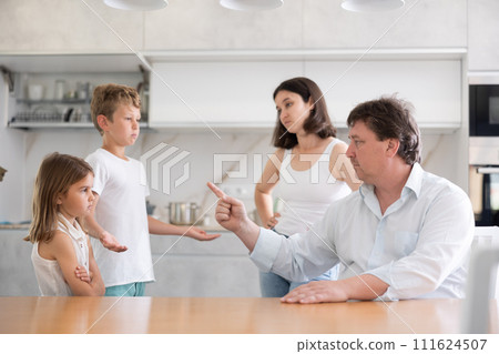 At home in kitchen, outraged mom and dad scold their son and daughter for disobedience. At home in kitchen, outraged mom and dad scold their son and daughter for disobedience. 111624507