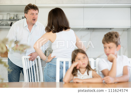 Brother and sister sit at table during quarrel between parents 111624574