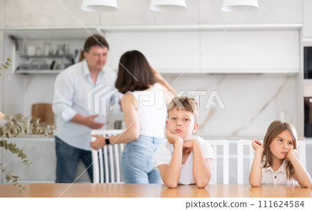 Family problem, conflict and people concept - sad children sitting at table their parents quarreling at home Family problem, conflict and people concept - sad children sitting at table their parents quarreling at home 111624584