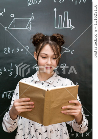 Girl reading a book standing at the blackboard, homework report in front of the school class Girl reading a book standing at the blackboard, homework report in front of the school class 111625116