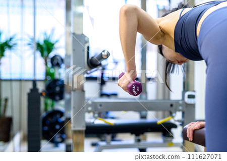 Young woman training her body at a personal gym, one-handed rowing, dumbbell row, muscle training girl, clearly 111627071