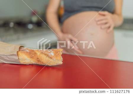 Pregnant woman eating bread in the kitchen. Exploring the impact of gluten during pregnancy: understanding the potential benefits and risks for maternal health and fetal development Pregnant woman eating bread in the kitchen. Exploring the impact of gluten during pregnancy: understanding the potential benefits and risks for maternal health and fetal development 111627176