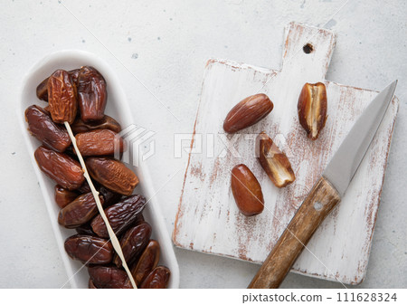 Organic dried sweet dates with chopping board and knife on white kitchen background. Organic dried sweet dates with chopping board and knife on white kitchen background. 111628324