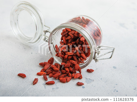Glass jar with dried red sweet goji berries on white kitchen background. Glass jar with dried red sweet goji berries on white kitchen background. 111628376