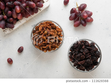 Two bowls with dried raisins with ripe red grapes on light background. 111628388