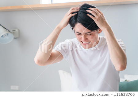 A young Asian man panics in his home/hotel bedroom (lateness, overslept, distress, regret, failure) 111628706