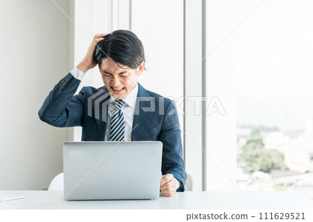 一位年輕的亞洲商人在辦公桌前工作，他很忙，做了一次手術，產能過剩，擔心壓力，並且遇到了麻煩。 111629521