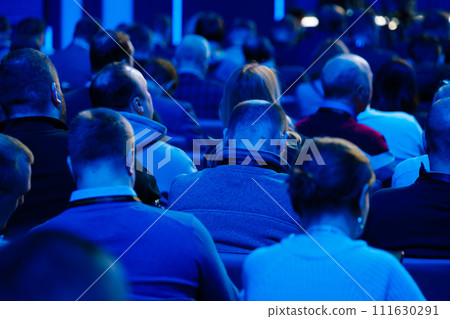 Audience at conference event listening to speaker in blue lit room 111630291