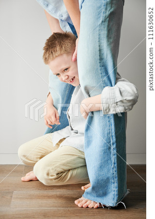 Young happy boy hugging mom's legs. Hyperactive kid holding his mother's legs. Clingy son wanting attention from mommy. 111630652