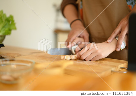 Woman hand chopping garlic on wooden board while preparing meal with her husband in the kitchen 111631394