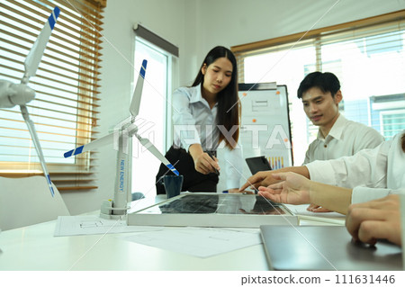 Team of eco engineers having a discussion while working with wind turbine models and solar panel at office 111631446