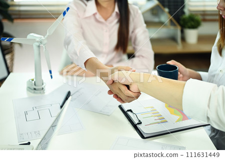 Businesswoman and engineer shaking hands over meeting table. Green energy development concept Businesswoman and engineer shaking hands over meeting table. Green energy development concept 111631449