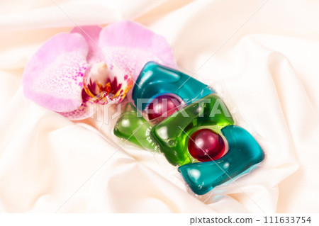 Laundry capsules among orchid flowers on satin fabric. 111633754
