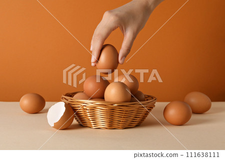 Eggs in a wicker basket, with a hand, on an orange background. 111638111