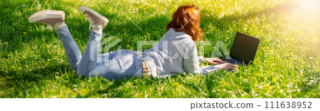 Woman lying with laptop on the blossoming meadow in natural park. Woman lying with laptop on the blossoming meadow in natural park. 111638952