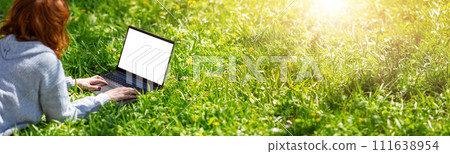 Woman lying with laptop on the blossoming meadow in natural park. 111638954